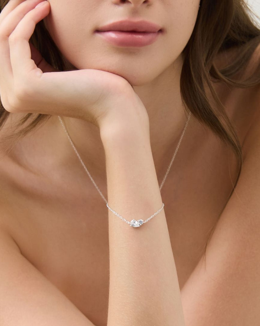 Woman wearing a delicate necklace with a clear pendant on a neutral background
