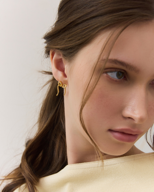 Close-up of a woman wearing gold earrings with a plain background
