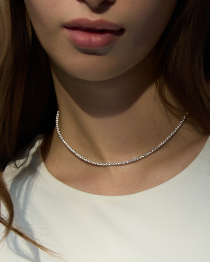 Close-up of a person wearing a delicate silver necklace against a neutral background