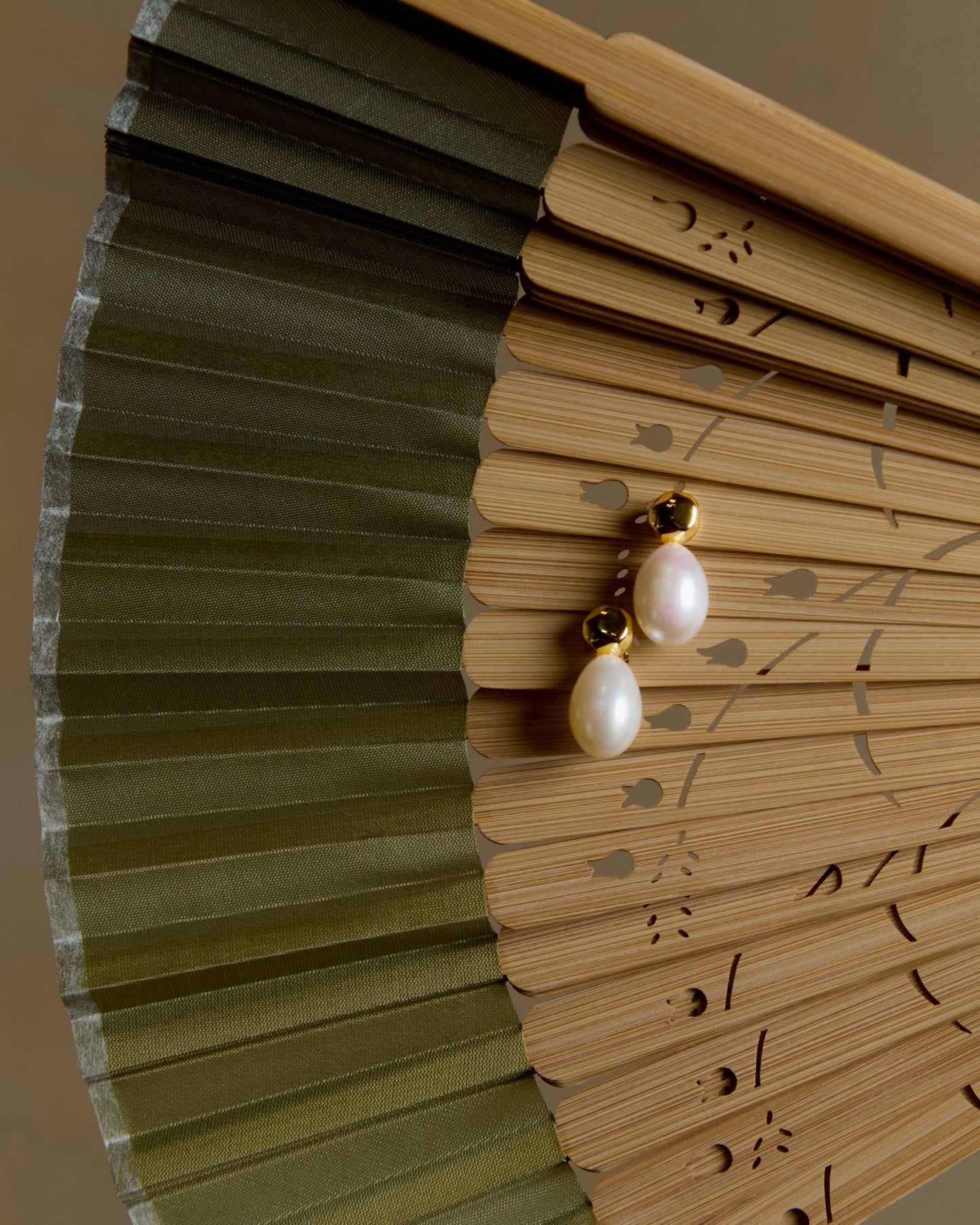 Pearl earring on a wooden fan with green leaves