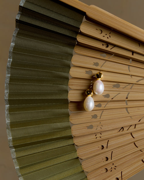 Pearl earring on a wooden fan with green leaves
